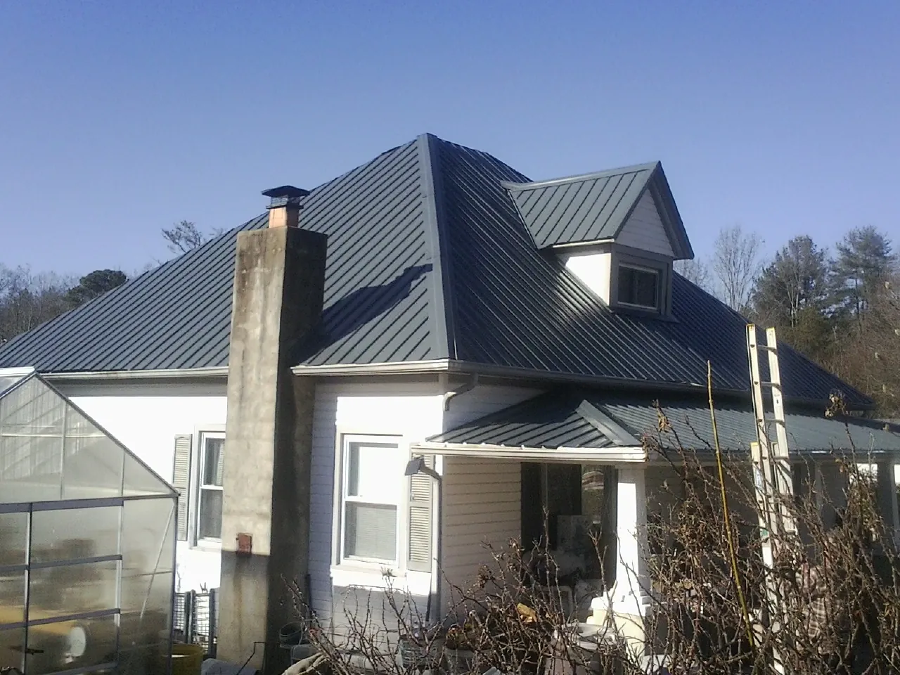 Dark blue standing seam metal roof on a white farmhouse with dormer — Slate & Tile Roof Repair by Roofing Brothers in Pilot