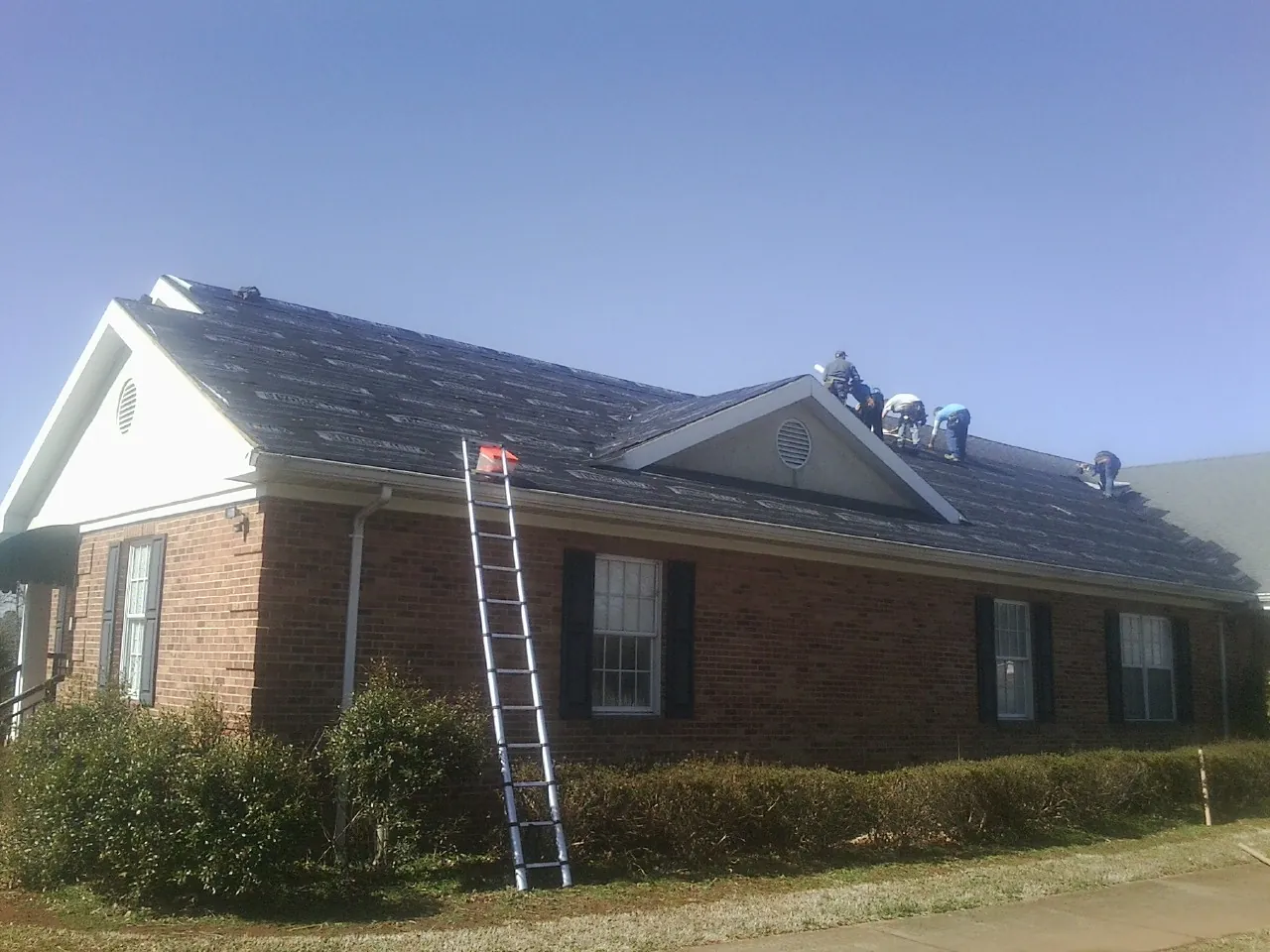 Crew tearing shingles off a brick ranch roof with a ladder set — Metal Roof Repair work by our crew in Pilot