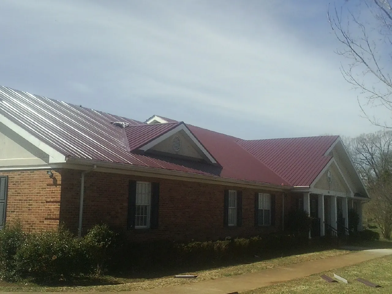 Red metal roof with gabled entries on a long brick building, from a Hail Damage Roof Repair job in Pilot