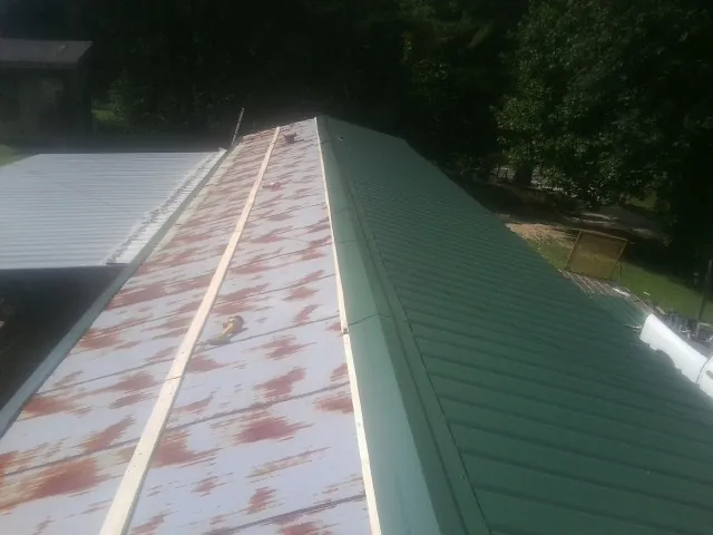Old rusted panels beside newly installed green metal roofing — Wind Damage Roof Repair by Roofing Brothers in Pilot