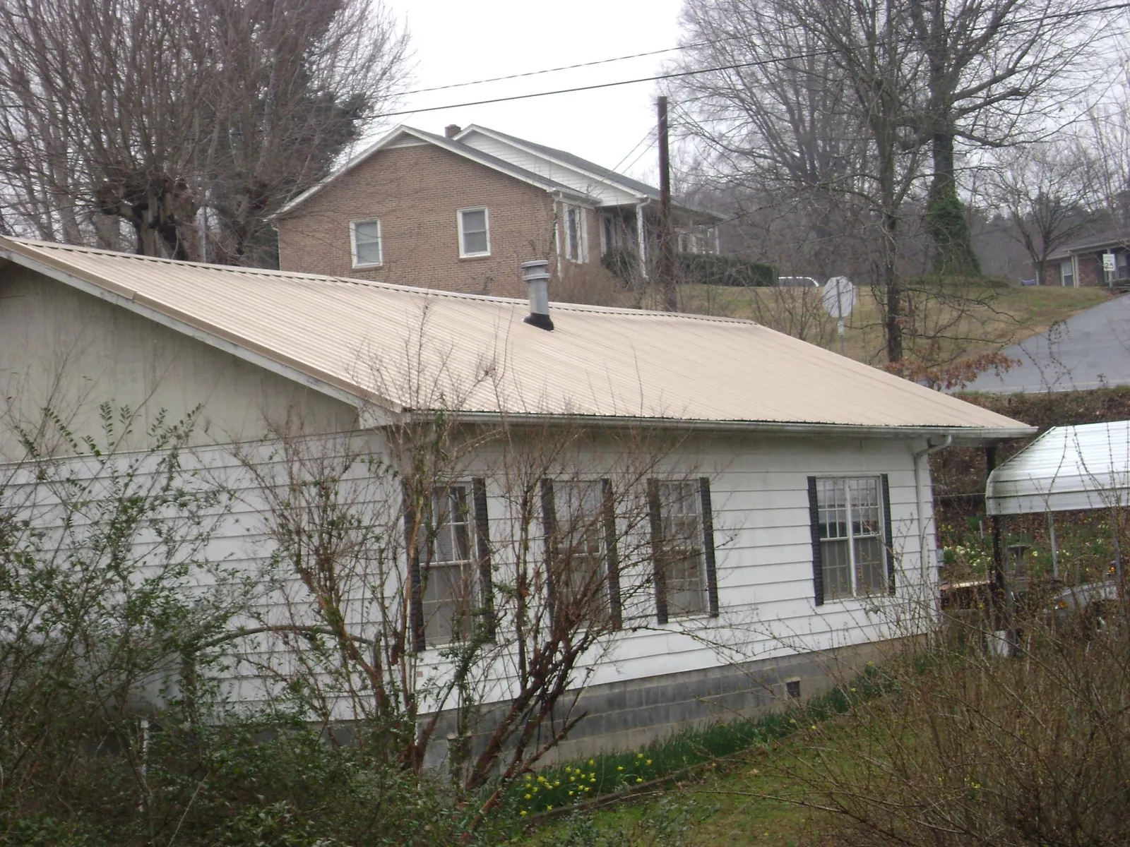 Tan metal roof on a white sided house set into a hillside — Commercial Roofing by Roofing Brothers in Pilot
